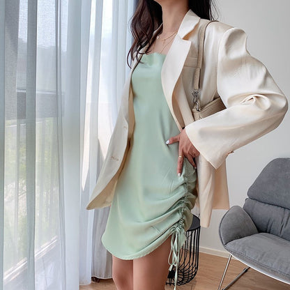 Woman is wearing a green mini slip dress wwith a jacket standing near a window with white curtain| VYEN
